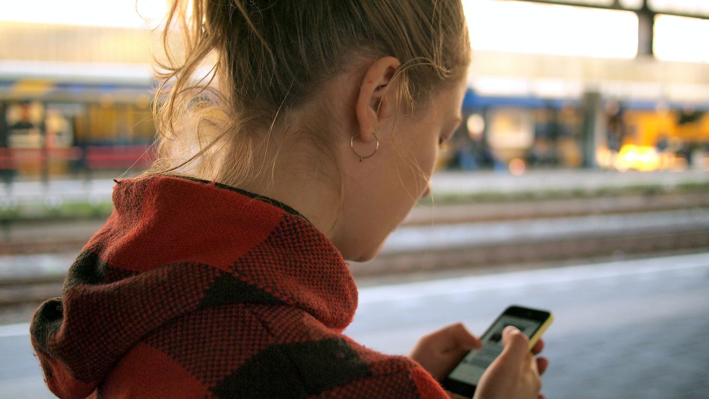 A young woman typing on her phone at a train station